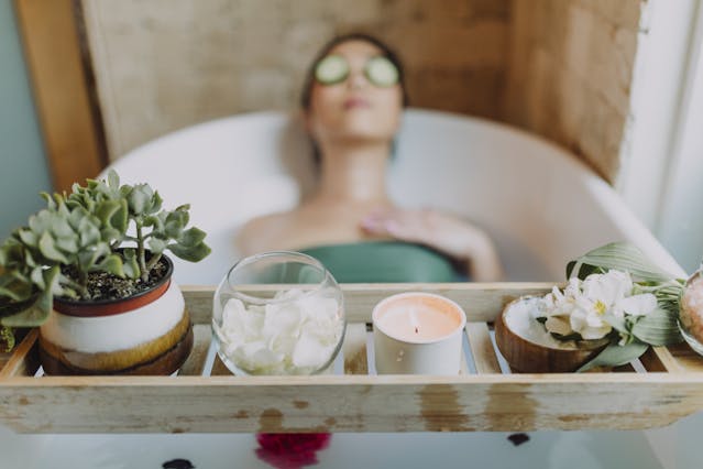 Woman relaxing in a bathtub with a candle and plants, enjoying a serene spa experience.