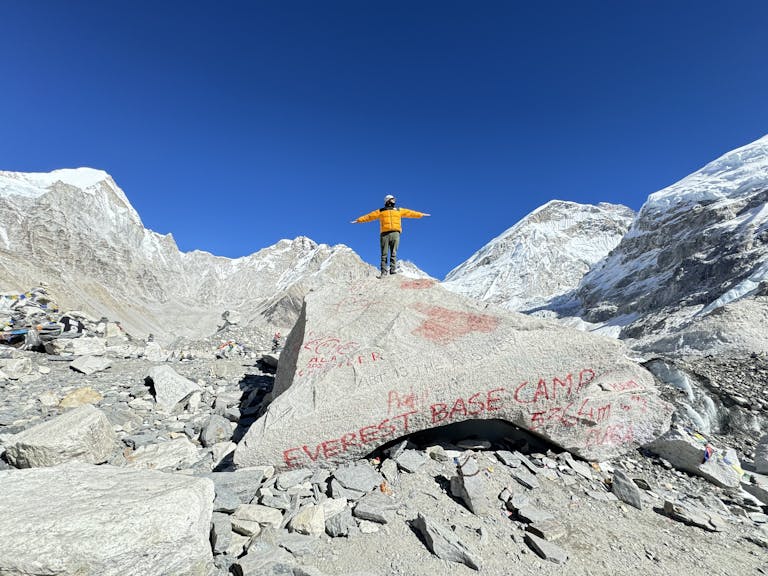 A mountaineer stands on a rock at Everest Base Camp, surrounded by snowy peaks.