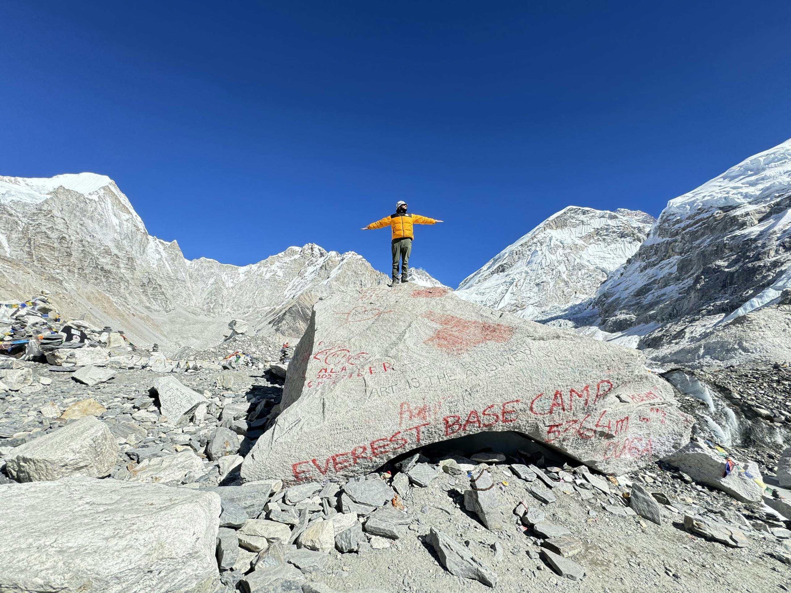 A mountaineer stands on a rock at Everest Base Camp, surrounded by snowy peaks.