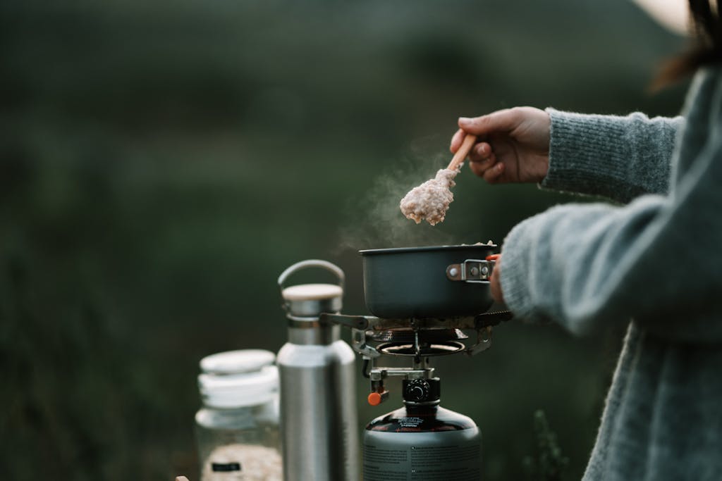 A person is cooking steaming oatmeal on a portable stove during a camping trip.